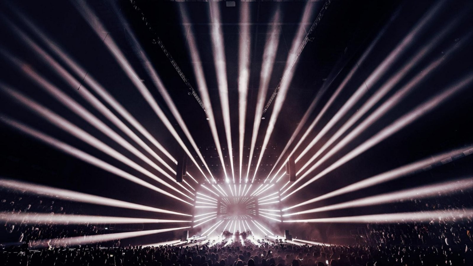 Image of a show within The O2 arena with white light coming from the centre of the stage to the back of the arena 