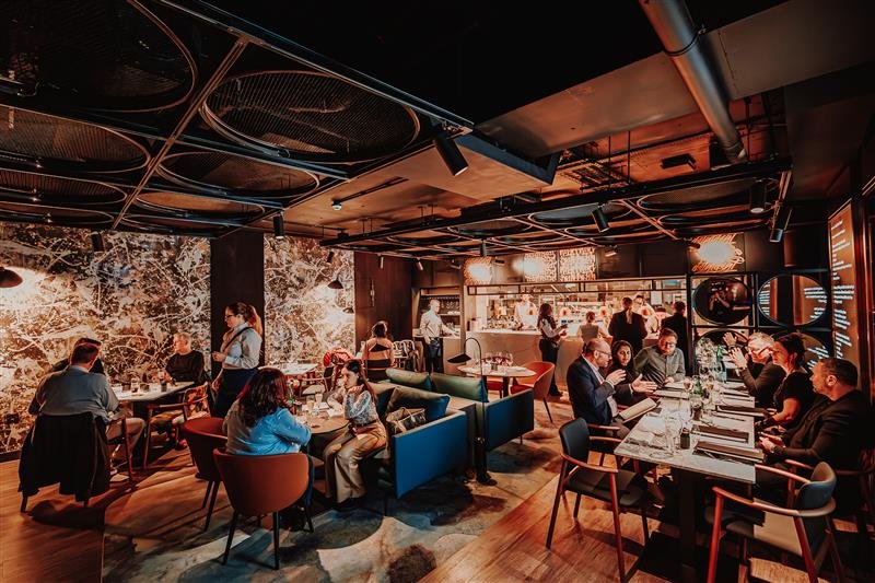 Image of The NinetyThird restaurant with dark lighting and groups of people enjoying a meal 